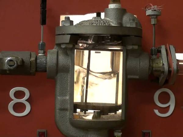 The steam trap with the asbestos gasket is working in front of the red wall.